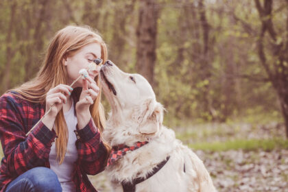 young woman feeding food to dog outside in the fall forest